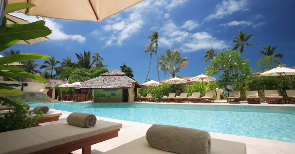Experience ultimate relaxation at a sunlit tropical poolside resort featuring palm trees and blue skies.